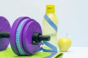 Concept of sport and healthy lifestyle. Training dumbbells, water, towel, apple on a blue background. photo