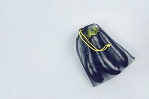 Eggplant in a black grocery bag on a gray background, top view and copy space