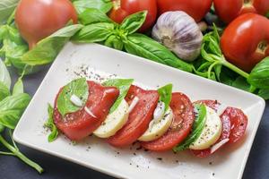 Comida tradicional italiana, tomates en rodajas y mozzarella y albahaca en una placa blanca. foto