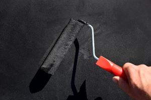 painting the surface in black with a brush roller.man's hand holds brush roller