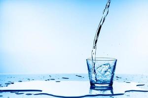 Verter agua en un vaso sobre fondo azul. foto