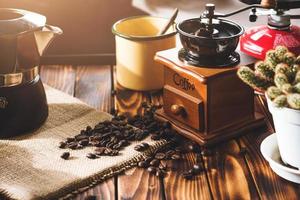 taza de café, granos tostados e ingredientes para hacer café y accesorios en el fondo de madera de la mesa. concepto de fabricación de café foto