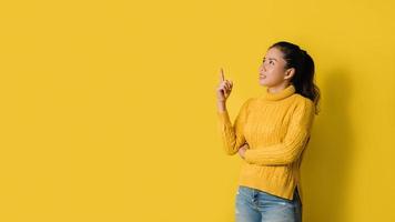 Portrait of an excited young blonde girl pointing with hand and finger to the side looking on yellow background. Pointed to the presentation. Space for text
