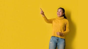 Portrait of an excited young blonde girl pointing with hand and finger to the side looking at the camera over yellow background. Pointed to the presentation. Space for text photo