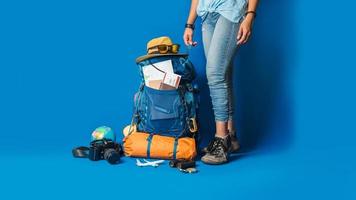 Tourist planning vacation with the help of world map with other travel accessories around. Woman traveler with suitcase on Blue color background. Concept travel backpack