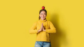 Cheerful young woman on yellow background in studio. A girl with an apple resting on her head while doing yoga. The concept of exercise for good health. Health lover photo