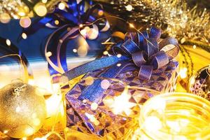 Christmas gift with blue ribbon and Christmas decoration balls on abstract bokeh black background with copy space and decorative LED lights. Merry Christmas and New Year.