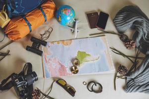 vacaciones de planificación turística con la ayuda del mapa del mundo con otros accesorios de viaje alrededor. teléfono inteligente, cámara de película y gafas de sol sobre un fondo blanco. mochila de viaje foto