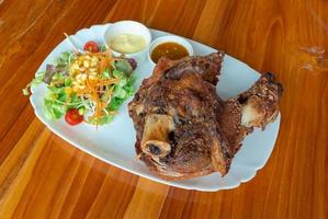 deep crispy fried pork knuckle or pork leg in German style with salad and sauce on wooden table photo