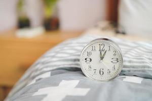 un reloj despertador redondo se encuentra en la manta al lado de la cama. diseño de dormitorio.
