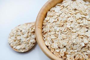 Close-up rolled oats in a wooden cup and spoon on white background. It is a healthy whole grain food. photo