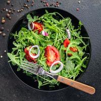 Ensalada de verduras frescas rúcula, tomate, plato de cebolla, comida, bocadillo en la mesa, espacio de copia, fondo de alimentos foto