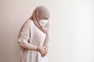 Muslim woman wearing a surgical mask feeling sick on pastel background. Covid-19 coronavirus concept. photo