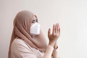 niña musulmana con una mascarilla quirúrgica rezando durante el trabajo desde casa. concepto de coronavirus covid-19. foto