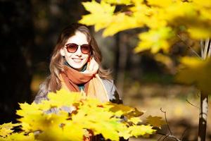 Hermosa mujer joven en gafas de sol entre hojas de otoño
