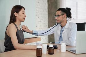 tratamiento médico y chequeo, un joven médico examina a una paciente de etnia asiática con un estetoscopio, aconseja una cita para una consulta de salud en una clínica de un hospital. foto