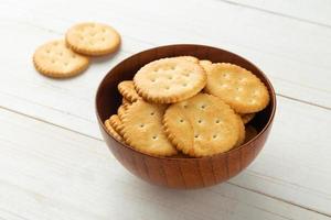 Rounded cracker cookies in a wooden bowl on white wooden table background photo