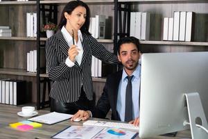 young middle east businessman sitting on chair and caucasian businesswoman standing beside her colleague in office. business concept photo