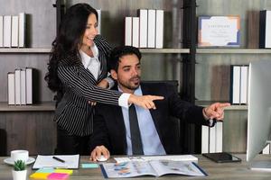 joven empresario de Oriente Medio sentado en una silla y empresaria caucásica de pie junto a su colega en la oficina. concepto de negocio foto