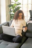 Latin woman using laptop and hand holding credit card for shopping on sofa photo