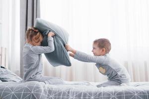 Little boy and girl staged a pillow fight on the bed in the bedroom. Naughty children beat each other pillows. They like that kind of game photo