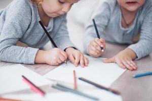 Children lie on the floor in pajamas and draw with pencils. Cute child painting by pencils. Hand of child girl and boy draw and paint with crayon. Close up view photo