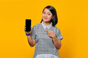 Smiling asian woman showing blank smartphone screen and pointing on it while looking at the camera photo