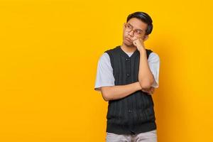 Portrait of thinking Asian man touching chin and looking at blank space over yellow background photo