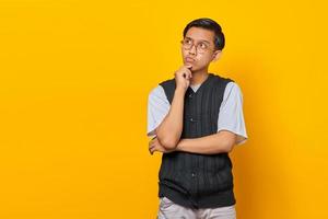 Pensive handsome young man rubbing chin and thinking question on yellow background
