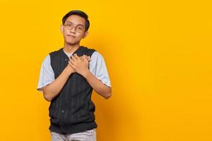 Happiness young Asian man keeping both palms on chest isolated over yellow background photo