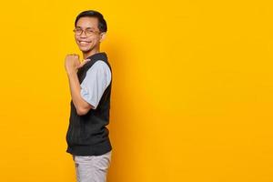 Handsome Asian man cheerful and pointing to empty space isolated on yellow background photo