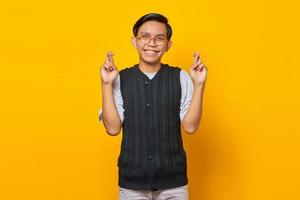 Portrait of smiling young asian man uniform gesturing finger crossed on yellow background photo
