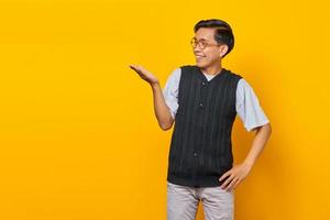 Portrait of smiling handsome young man showing copy space in palm on yellow background photo