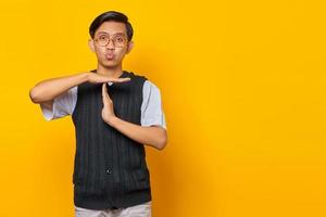 Portrait of young asian man showing timeout gesture on yellow background photo