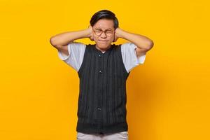 Frustrated Asian young man covering ears with hands isolated over yellow background photo