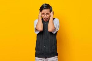 Frustrado joven asiático cubriendo los oídos con las manos aisladas sobre fondo amarillo foto