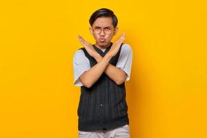 Serious young Asian man showing refusal gesture with crossed arms isolated over yellow background photo