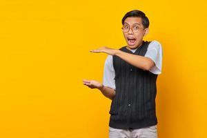 Hombre asiático sorprendido que muestra el producto sobre fondo amarillo foto
