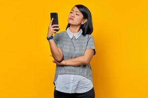 Joven mujer asiática que se siente molesta y enojada mientras mira el mensaje en el teléfono inteligente sobre fondo amarillo foto