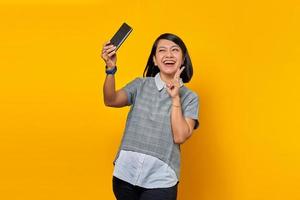 Portrait of cheerful young Asian woman using mobile phone take selfie make peace sign photo