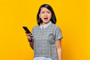 retrato, de, sorprendido, joven, mujer asiática, tenencia, teléfono móvil, en, fondo amarillo foto