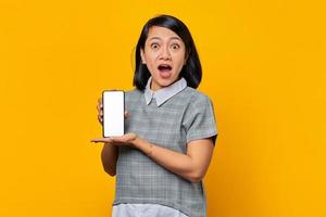 sorprendida mujer asiática que muestra la pantalla del teléfono inteligente en blanco con la palma. concepto de promoción de productos foto