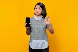 Portrait of surprised young Asian woman with open mouth showing blank screen smartphone and doing stop gesture with palms photo