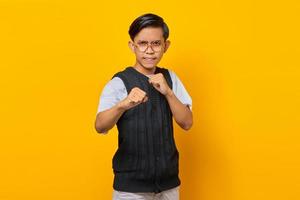 Portrait of angry young asian man showing boxer gesture on yellow background photo