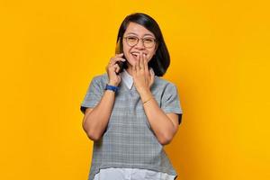 Happy young asian woman laughing while receiving incoming call on mobile phone and covering mouth with hands photo