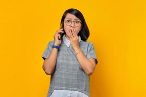 Surprised young Asian woman on receiving incoming call on mobile phone and covering mouth with hand photo