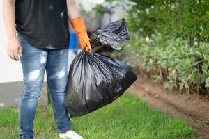 Mujer sosteniendo bolsas de basura de plástico negro de basura en el pavimento, concepto de medio ambiente limpio. foto