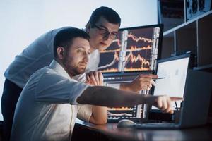 Team of stockbrokers are having a conversation in a dark office with display screens. Analyzing data, graphs and reports for investment purposes. Creative teamwork traders photo