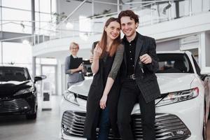 Now her dream comes true. Two happy young attractive owners of car, elegant salesperson at background