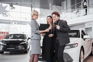 Proud owners. Beautiful young happy couple hugging standing near their newly bought car smiling joyfully showing car keys to the camera copyspace family love relationship lifestyle buying consumerism